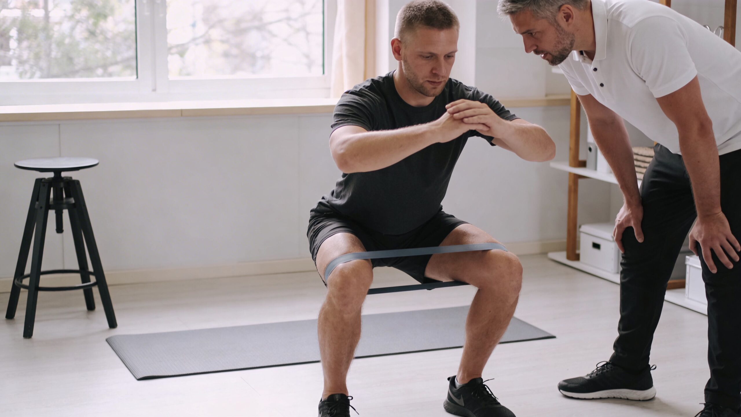 A patient with knee pain performing squats with a resistance band under the supervision of a physical therapist.